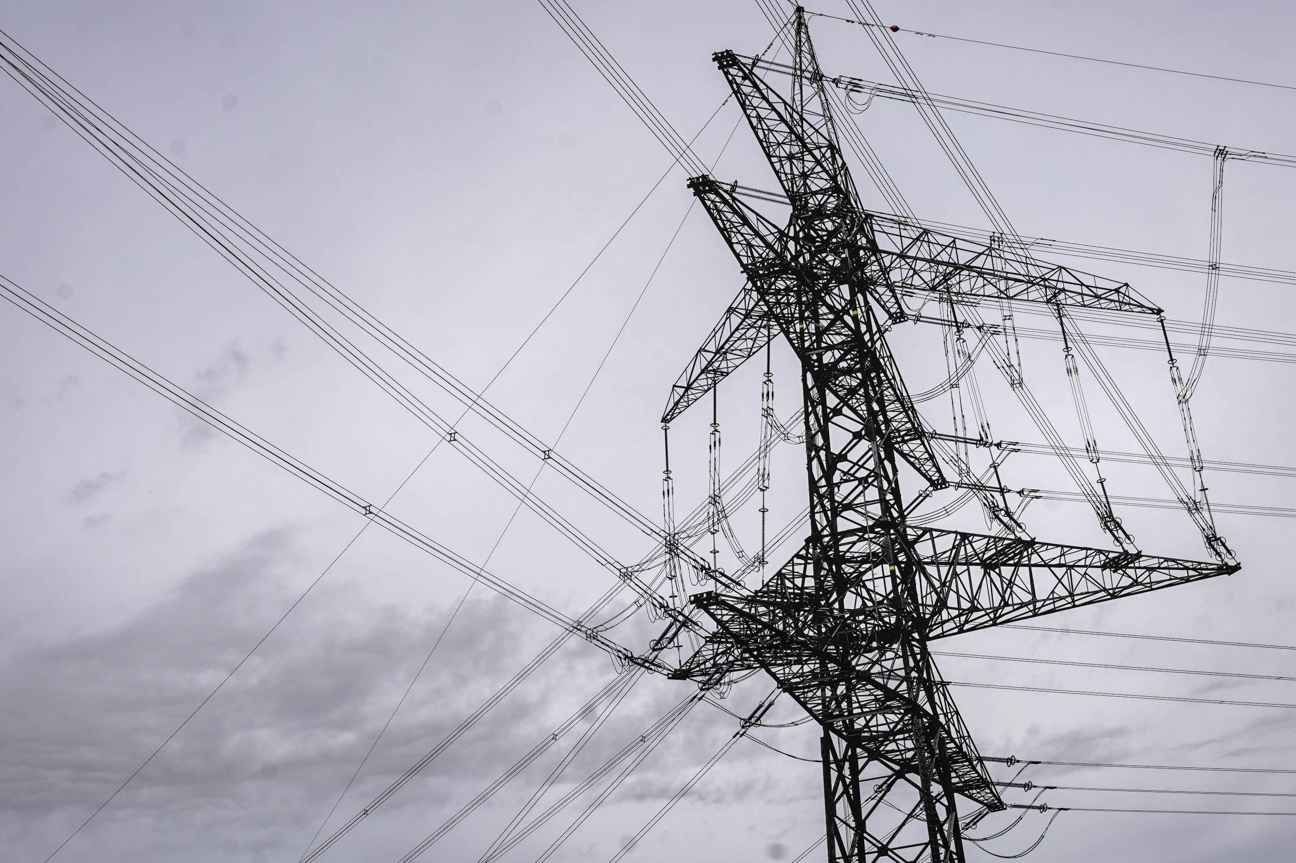 Höchstspannungsmast aus Stahl mit mehreren Querträgern und zahlreichen Stromleitungen gegen bewölkten Himmel. 